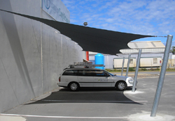 Flat carport shade sail using wall mounts and posts.